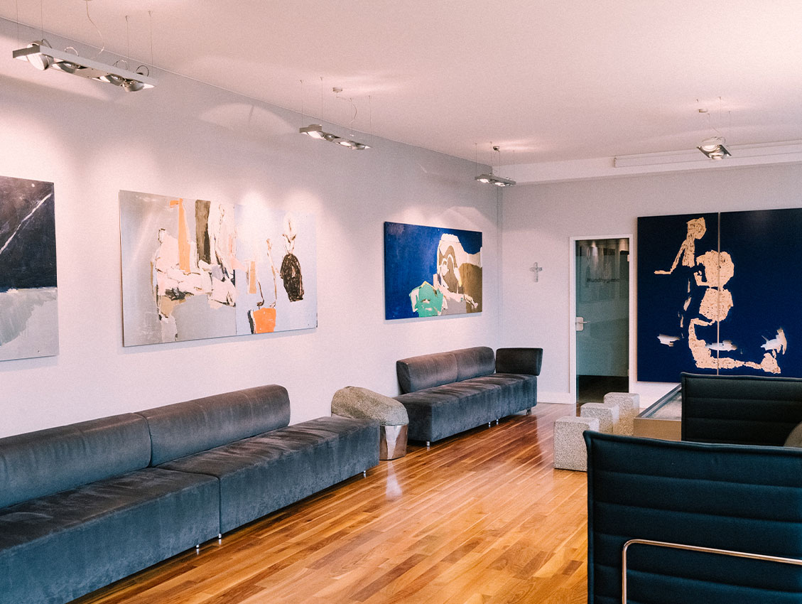 Kieferorthopädie Deggendorf – Moderner Wartebereich der Kieferorthopädie-Praxis ARTPRAXIS® in Deggendorf mit stilvollen Kunstwerken, Designermöbeln und Parkettboden – entspannte Atmosphäre für Patient:innen.