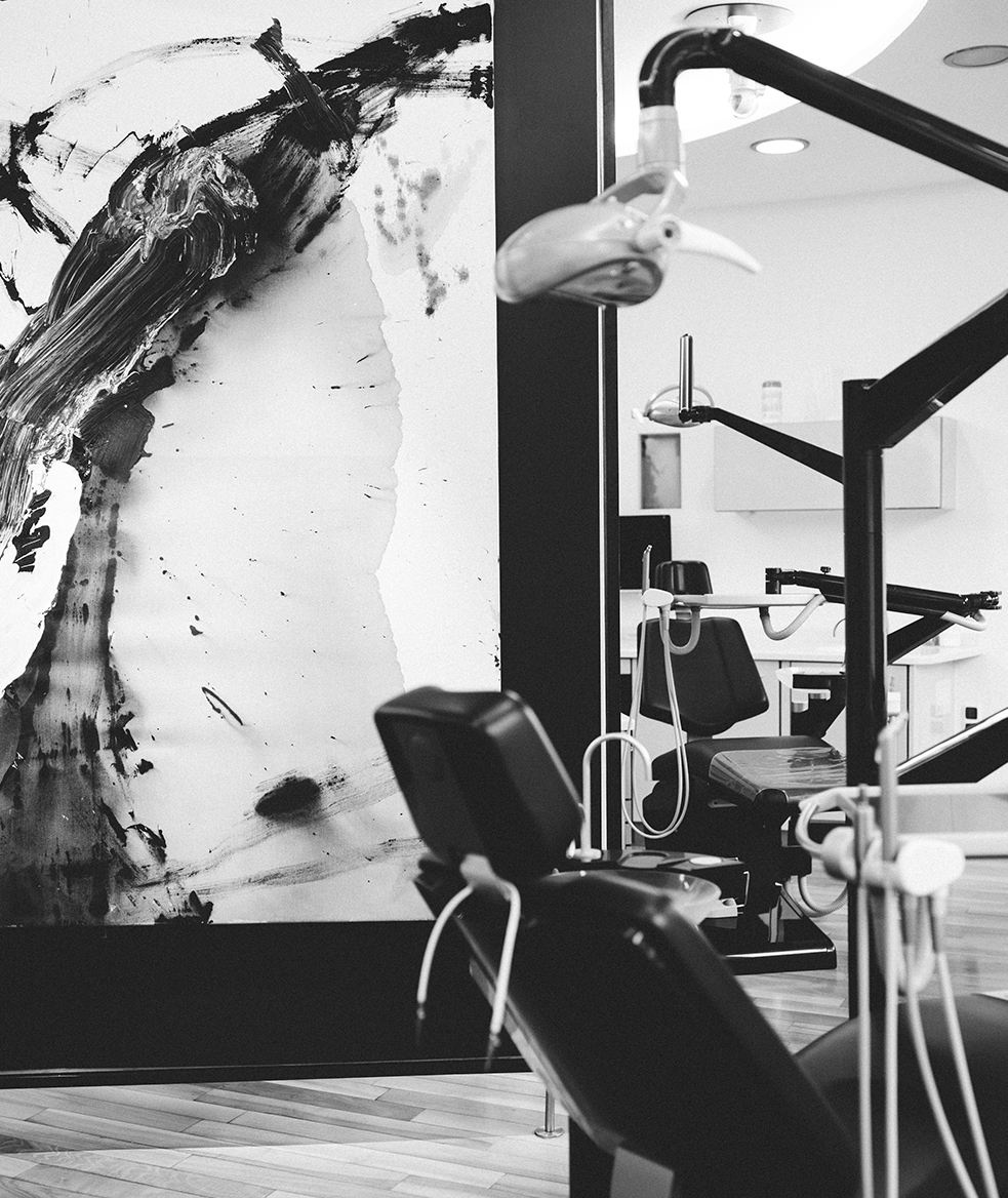 Kieferorthopädie Deggendorf – Moderne kieferorthopädische Behandlungseinheit in einem lichtdurchfluteten Praxisraum, im Vordergrund eine abstrahierte Schwarz-Weiß-Malerei als gestalterisches Element – das Bild verbindet medizinische Präzision mit künstlerischem Anspruch.