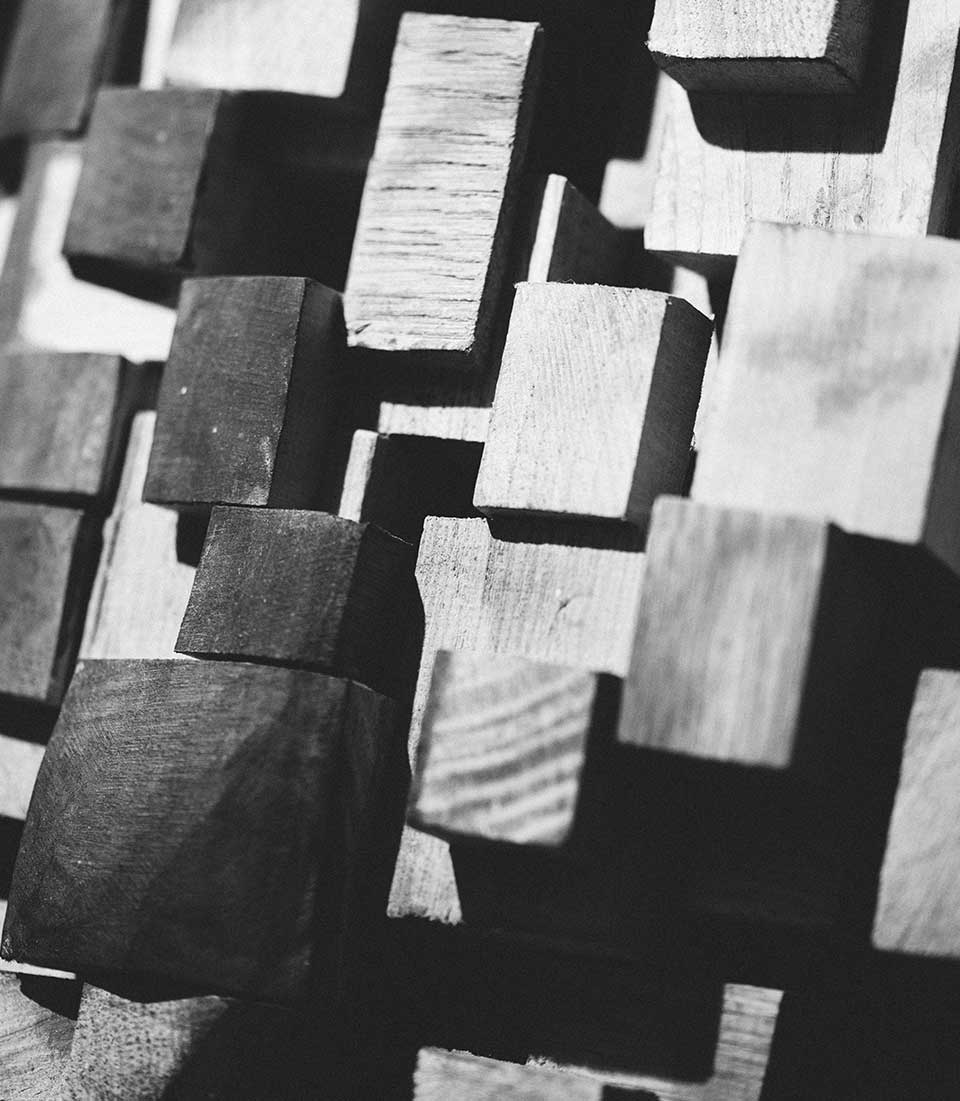 Kieferorthopädie Deggendorf – Nahaufnahme einer skulpturalen Holzinstallation aus unterschiedlich großen, hervorstehenden Holzquadern; das Schwarz-Weiß-Bild betont Struktur, Tiefe und das Spiel von Licht und Schatten.