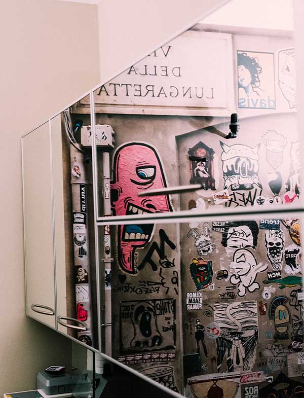 Kieferorthopädie Deggendorf – Spiegelung einer bunt beklebten Wand mit urbaner Streetart, darunter auffällige Illustrationen, Schriftzüge und Sticker; fotografiert in einem Praxisraum mit modernem Interieur.